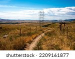 High voltage power line on open grassy plain with steel pylon next to Dakota Hogback against blue sky with white clouds