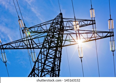 a high voltage power pylons against blue sky and sun rays