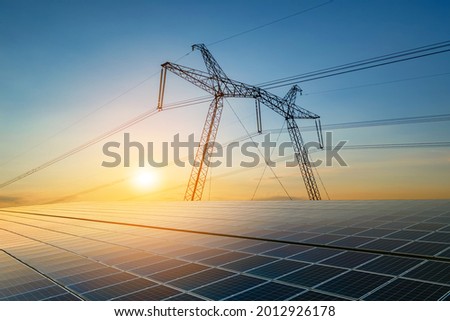 High voltage pylons with electric power lines transfering electricity from solar photovoltaic sells at sunrise. Production of sustainable energy concept. Stockfoto © 
