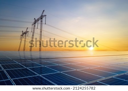 High voltage pylons with electric power lines transfering electricity from solar photovoltaic sells at sunrise. Production of sustainable energy concept.