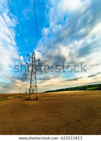 High voltage tower in the countryside. The blue sky with clouds and the field in culture will leave the landscape.