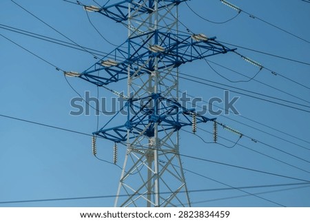 High voltage transmission tower with multiple power lines against clear blue sky, close view showing lattice structure, insulators, crossarms, and cable span, with transmission, tower, power, line
