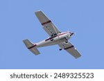 High wing aircraft flies by at low altitude. Propeller driven piston powered airplane isolated on blue sky baackground. White paint and red stripe