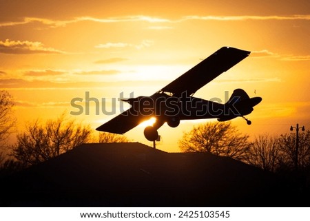 high wing airplane silhouette coming in for landing at sunset