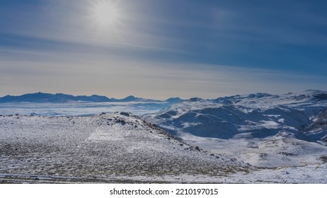 From the high-altitude plateau there is a view of endless expanses. A snow-covered mountain range against a blue sky. The rays of the sun shine in the firmament. Altai - Shutterstock ID 2210197015