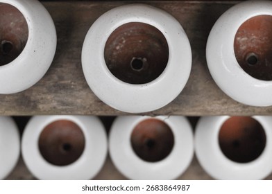 High-angle abstract close-up of two rows of small, empty white-glazed terracotta pots on a weathered wooden shelf, highlighting the circular pattern of the openings and drain holes.