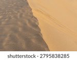 A high-angle abstract shot showcasing the sharp contrast of bright sunlight and deep shadow on textured desert sand dunes in Qatar.