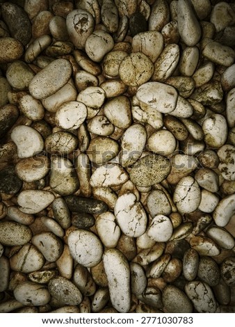 a high-angle, close up shot capturing a dense collection of smooth, rounded river stones or pebbles. The composition is filled entirely by these stones, creating a textured and natural pattern that covers the entire frame