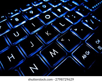 High-angle close-up of a backlit computer keyboard glowing with bright blue light in a dark room