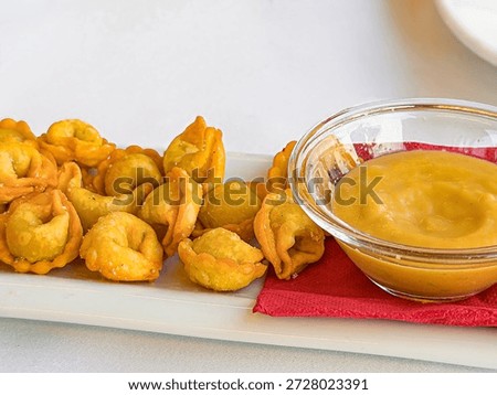 High-angle close-up of crispy deep-fried tortellini snacks served on a white rectangular plate with a side of yellow dipping sauce. This mouth-watering food photography is perfect for restaurant menus, catering services, culinary blogs, and food industry advertising.