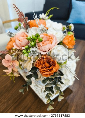 High-angle close-up of an elegant artificial flower bouquet featuring white, peach, and burnt orange faux roses arranged with green foliage on a wooden table.
