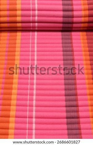 A high-angle close-up of a rolled beach mat with a ribbed texture and striped pattern in shades of pink, orange, and white