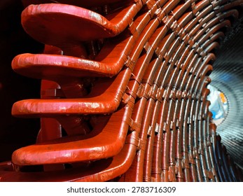​A high-angle, close-up shot captures the complex, repetitive structure of heavy-duty industrial stator windings inside a large electric motor or generator. The thick, curved copper bars are meticulously wrapped in protective insulation tape and coated with a glossy, reddish-orange insulating varnish. The overlapping coils create a striking geometric pattern that leads the eye toward the cylindrical core of the machine. The dramatic lighting highlights the shiny texture of the varnish and emphasizes the immense scale and precise engineering of this industrial power equipment.