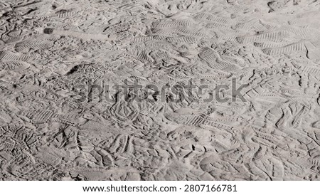A high-angle, close-up shot of multiple overlapping shoe print impressions in dry, textured sand, illustrating a busy path or high-traffic area.