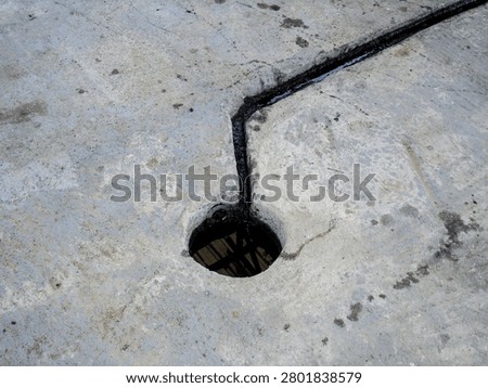 A high-angle, close-up shot showing thick, black leaked waste oil channeling through a groove on a grey concrete surface and draining down into a circular industrial floor opening.