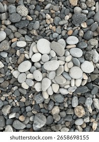 High-angle close-up showcasing an assortment of smooth pebble stones arranged closely together. The stones display a range of gray tones and soft textures, suitable for backgrounds