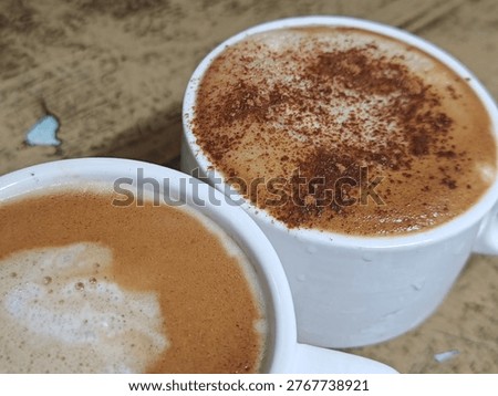 High-angle close-up of two cups of hot cappuccino and latte with creamy froth and cinnamon powder topping on a rustic wooden table
