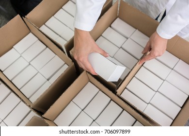 High-angle Close-up View Of The Hands Of A Manufacturing Worker Putting Packed Products, In Cardboard Boxes Before Export Or Shipping During Manual Work In A Cosmetics Factory