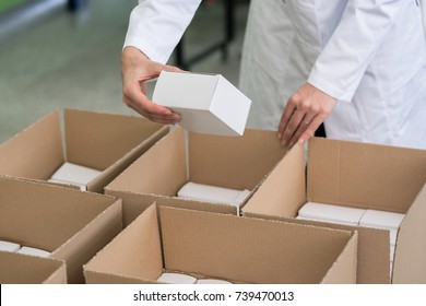 High-angle close-up view of the hands of a manufacturing worker putting packed products in cardboard boxes, before export or shipping during manual work in a cosmetics factory