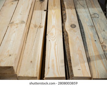 A high-angle close-up view of several stacked raw pine wood planks showcasing natural grain patterns, knots, and rough-cut edges in a warehouse setting.
