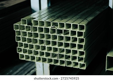 A high-angle close-up view of stacked square hollow steel tubes stored in a material warehouse. The image showcases the raw industrial texture of the metal, highlighting the geometric grid pattern formed by the ends of the pipes. Ideal for backgrounds related to construction, engineering, and heavy industry supply chains.