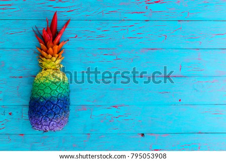 High-angle close-up view of a whole pineapple painted in stripes of vivid colors on a rustic blue wooden table