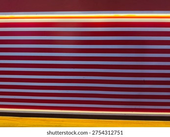 A high-angle close-up of a wall featuring horizontal red and white stripes illuminated by a warm yellow glow from an overhead light fixture