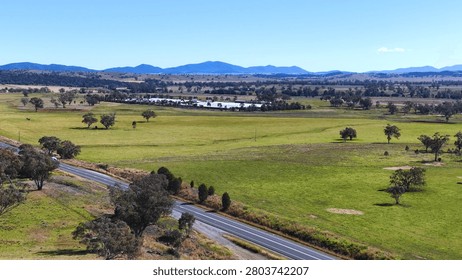 A high-angle drone shot captures a paved road winding through expansive green pastures in Armidale.