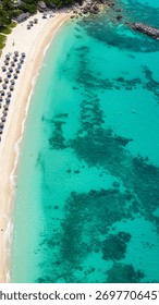 High-angle drone shot capturing a pristine tropical beach, white sand, and vibrant turquoise water.