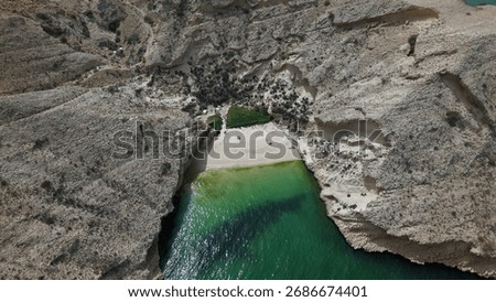 High-angle drone shot looking straight down at a secluded pocket beach framed by rugged limestone cliffs and emerald-to-turquoise water near Muscat, Oman. Graphic composition, natural textures and str