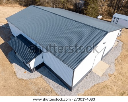 A high-angle drone shot showcasing the clean lines and sleek texture of a modern charcoal gray standing seam metal roof. The aerial perspective highlights the professional installation, ridge caps, and siding of a large commercial or utility building.