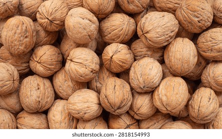 A high-angle, full-frame background texture featuring a dense pile of whole, raw walnuts in their intact brown shells. The top-down view highlights the deep, wrinkled organic patterns, distinct ridges, and natural variations across the hard wooden shells of the gathered nuts.