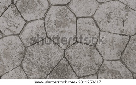 High-angle full-frame shot of a weathered gray stamped concrete floor with an irregular hexagonal stone pattern. The texture shows a rustic, grimy, and aged surface, ideal for background or architectural design concepts.