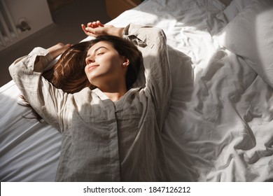 High-angle Of Girl Sleeping In Bed, Smiling And Looking Relaxed. Woman Lying In Bedroom, Enjoying Morning Sun.