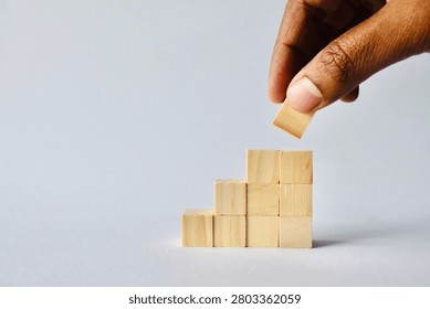 A high-angle horizontal composition showing a person's hand adding the final wooden block to an escalating staircase structure, symbolizing data growth or milestone completion.