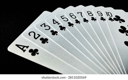 High-angle macro shot of a complete suit of clubs playing cards, fanned out from Ace to Ten, set against a sleek black textured background.