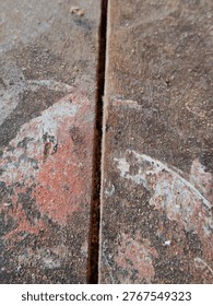 High-angle macro shot showing the joint of two rustic wooden boards. The surface is covered in fine wood dust and remnants of old red and white paint, creating a gritty, authentic industrial texture. Perfect for backgrounds related to woodworking, construction, or DIY home renovation.