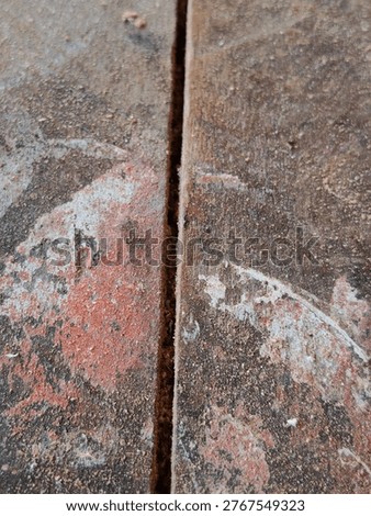 High-angle macro shot showing the joint of two rustic wooden boards. The surface is covered in fine wood dust and remnants of old red and white paint, creating a gritty, authentic industrial texture. Perfect for backgrounds related to woodworking, construction, or DIY home renovation.