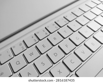 High-angle monochrome macro view of a white laptop QWERTY keyboard layout, focusing on key details, modern typography, and clean computer hardware design.