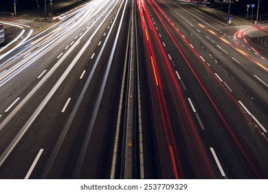 High-angle nighttime long-exposure shot of a highway, showing only the road and blurred car lights. Red and white light trails streak across the asphalt, capturing the dynamic energy of urban life. - Powered by Shutterstock