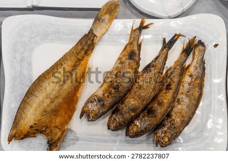 A high-angle overhead shot of a white ceramic platter holding one split-open premium barley-dried yellow croaker and four whole grilled yellow croakers, a hallmark of Korean regional cuisine.
