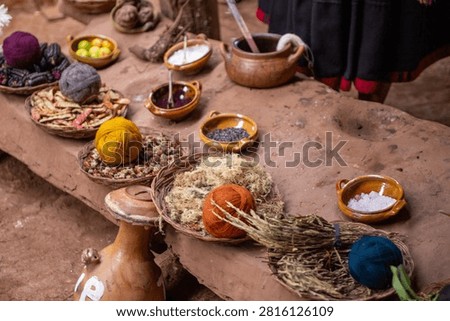High-angle overview of an artisan textile dyeing table in Peru, displaying ceramic bowls of powders and woven baskets with colorful wool yarn balls and local botanical ingredients.