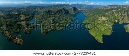 A highangle panoramic landscape of a winding river flowing through lush green tropical mountains and dense forest under a clear blue sky ideal for travel and environmental projects.
