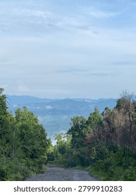 High-angle panoramic view looking down from a high hill or mountain, showcasing distant green valleys and foggy horizons.