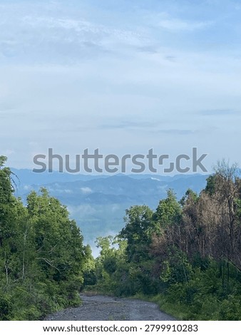 High-angle panoramic view looking down from a high hill or mountain, showcasing distant green valleys and foggy horizons.