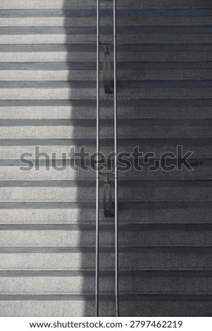 A high-angle perspective captures the textured surface of outdoor granite steps, bisected by a stark shadow and a central metal railing