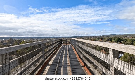 A high-angle perspective of a timber bridge path leading toward a scenic Australian landscape.