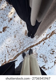 A high-angle point of view (POV) of two people standing on a snow-covered ground with dry pine needles.