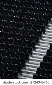 A high-angle, repetitive geometric pattern of empty black plastic stadium seats arranged in tiers, flanked by concrete stairs with visible row numbers.