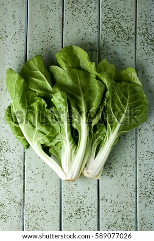 high-angle shot of a bunch of raw chard leaves on a rustic pale green wooden table